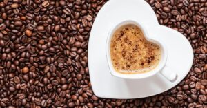 Espresso served in a heart-shaped cup amidst a bed of coffee beans, showcasing rich coffee aroma and style