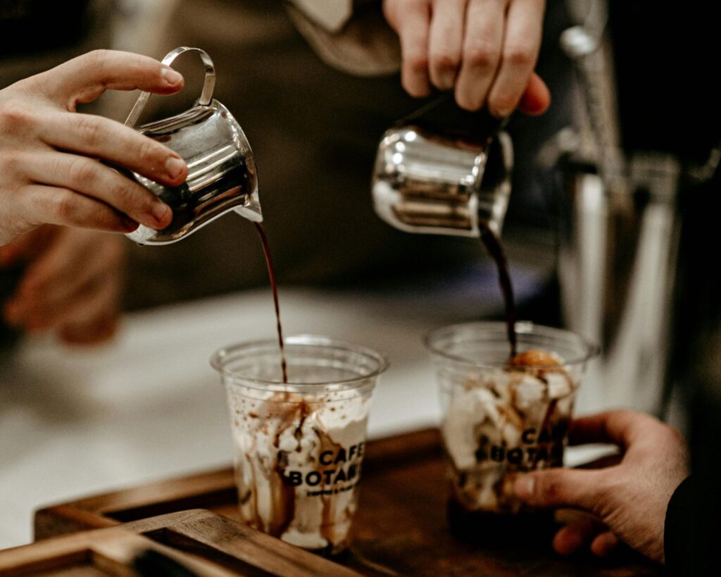 Espresso being poured into two cream-filled branded cups.