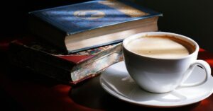 White Teacup with coffee And Saucer Beside Books