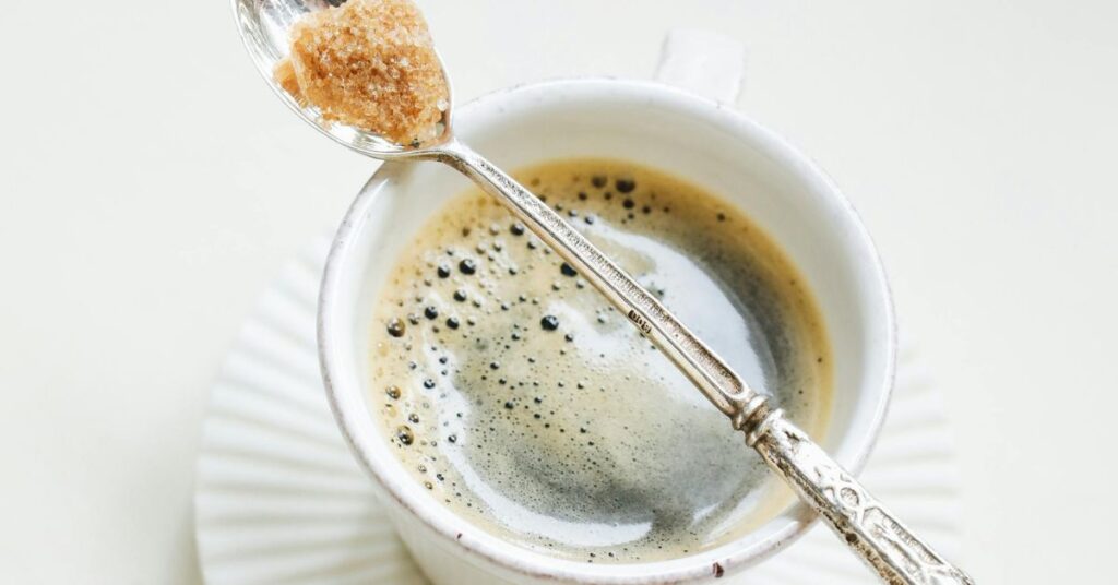 Spoon with brown sugar sitting on top of black coffee in a mug